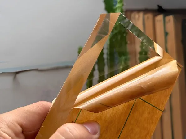 cận cảnh mép tấm nhựa PMMA trong suốt còn màng giấy bảo vệ